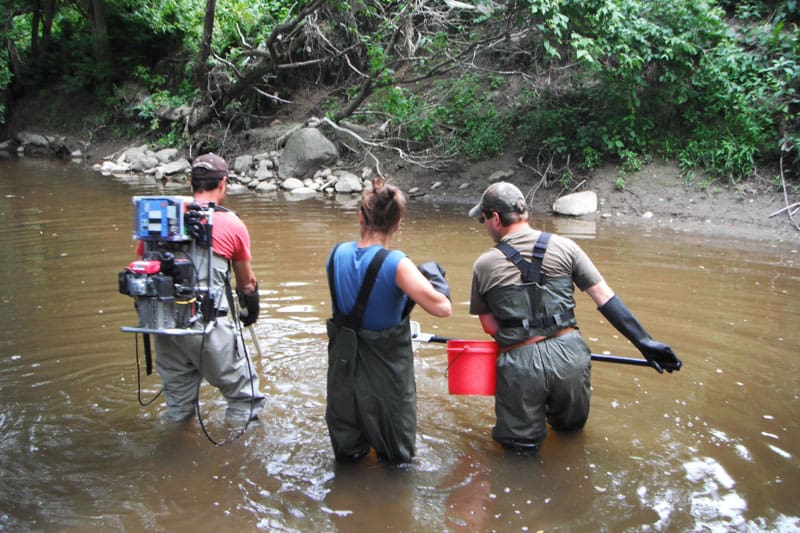 Scientifiques étudiant un ruisseau avec équipement spécialisé.