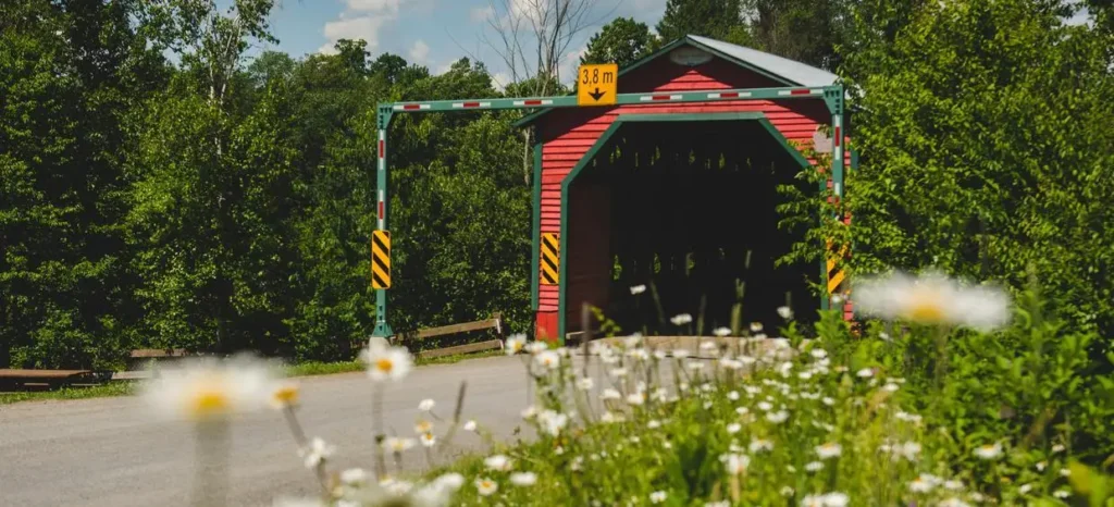 Pont couvert entouré de verdure et fleurs.