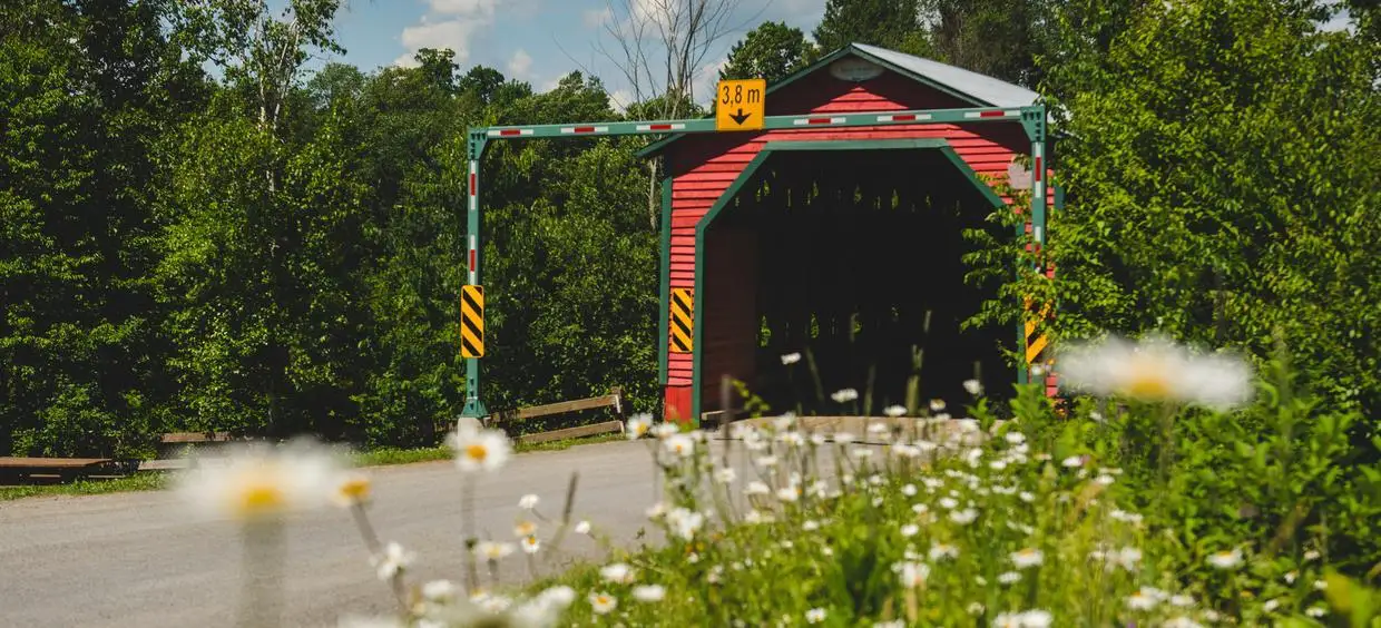 Pont couvert entouré de verdure et fleurs.