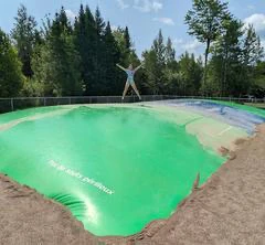 Personne sautant sur coussin gonflable vert, forêt derrière.
