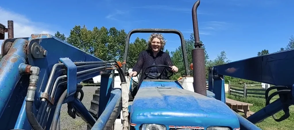 Personne conduisant un tracteur bleu dans une ferme
