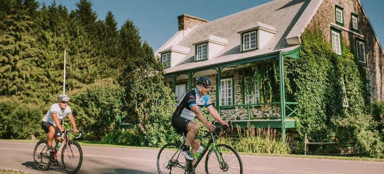 Cyclistes devant une maison en pierre verte.