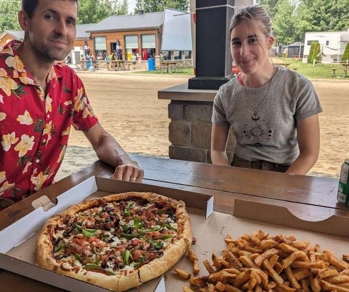 Deux personnes avec pizza et frites en extérieur.