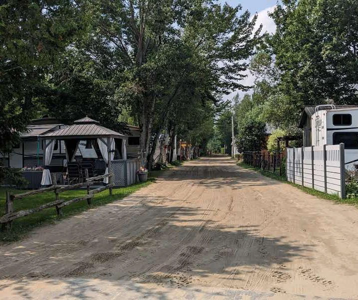 Rue de camping avec caravanes et arbres.