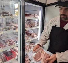 Boucher présentant de la viande devant réfrigérateur.