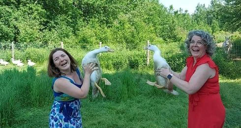 Deux femmes souriantes tenant des oies dans un pré.