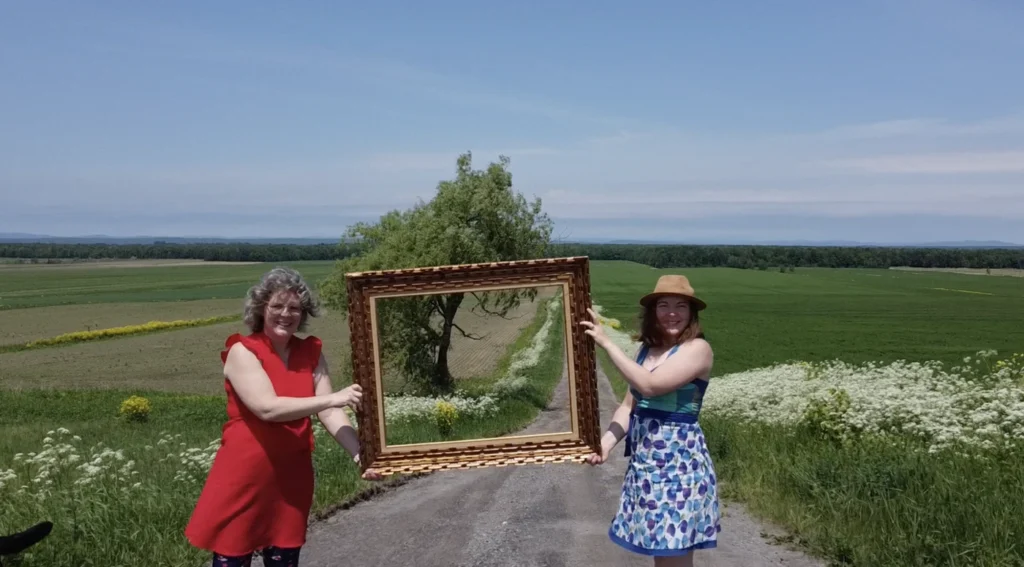 Deux femmes tenant un cadre vide dans un champ.