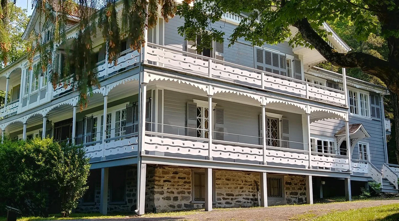 Maison victorienne bleue avec porches et volets fermés.