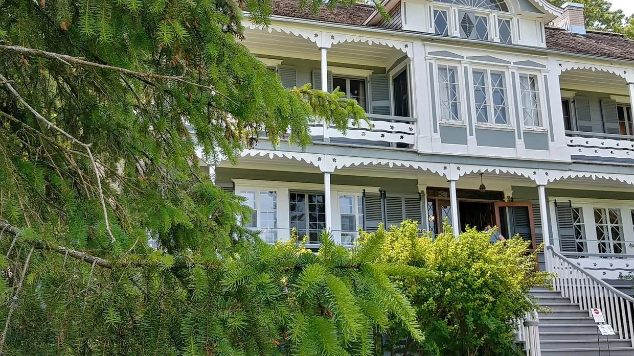 Maison en bois avec balcon, entourée d'arbres verts.