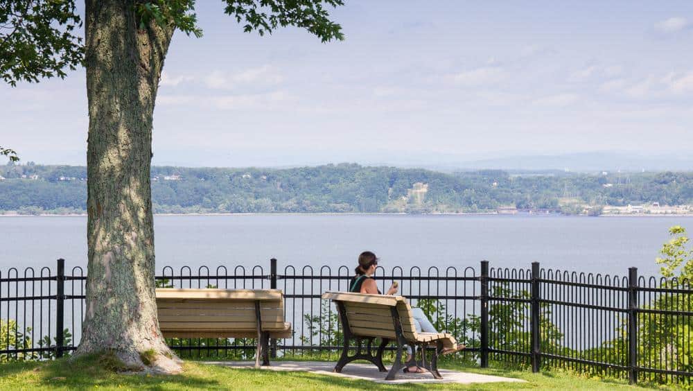 Femme assise sur un banc, vue sur rivière.
