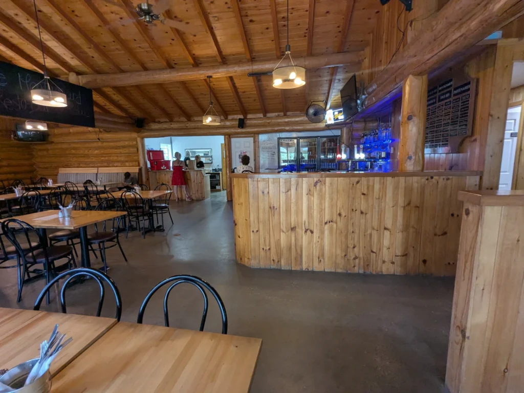 Intérieur d'un restaurant en bois, tables vides, bar visible.